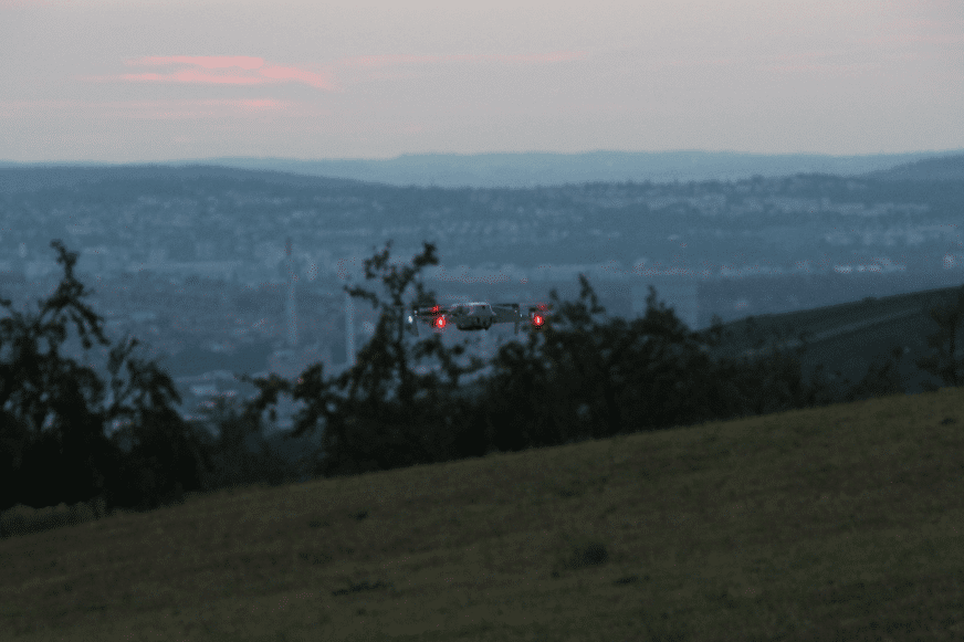 Die DJI Air 2S fliegt bei Dämmerung und die LEDs an den Armen der Propeller leuchten auf.